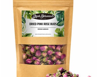 Może przedstawiać: Brązowa papierowa torba z przezroczystym okienkiem, w którym widać suszone różowe pąki róż. Etykieta głosi "Drink Botanicals Ireland" i "Dried Pink Rose Buds". Mały stos pąków róż leży przed torbą.