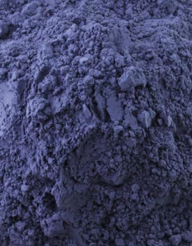 May include: Close-up of a pile of finely ground, deep blue powder. The powder has a textured, granular appearance, with varying shades of blue creating depth and dimension. The image is well-lit, highlighting the texture.