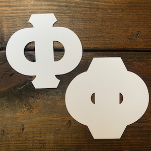 May include: Two white paper cutouts of the Greek letter Phi. The cutouts are on a brown wooden surface.