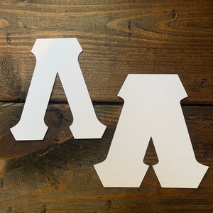 May include: Two white paper letters, both shaped like the letter A, are placed on a brown wooden surface.