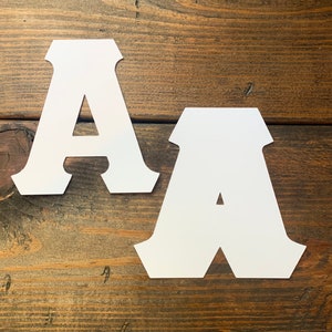 May include: Two white paper letters, both the letter A, on a brown wooden surface.