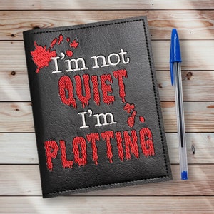 May include: Black leather notebook with red embroidered text that reads "I'm not quiet I'm plotting".
