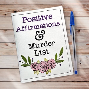 May include: A white notebook with the text "Positive Affirmations & Murder List" in black and purple embroidery. The notebook is decorated with a floral design of pink and yellow roses and green leaves.