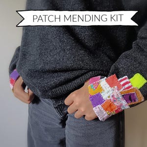 Może przedstawiać: Osoba w ciemnoszarym swetrze z kolorowymi mankietami w stylu patchwork. Mankiety wykonane są z różnych skrawków materiału w odcieniach różu, fioletu, pomarańczu, czerwieni i zieleni. Tekst "PATCH MENDING KIT" jest wyświetlany nad osobą.