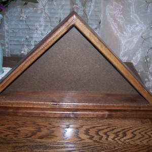 May include: A wooden shadow box with a brown felt lining, designed to display a folded American flag.