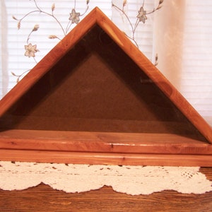 May include: A wooden triangular shadow box with a glass front and a brown felt lining. The box is designed to hold a folded American flag.