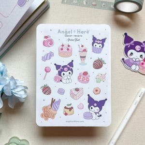 Op de afbeelding: Een stickerblad met de tekst "Angel + Hare Sweet Treats" met illustraties van desserts en een paars personage. Ook een aparte sticker van het personage met een cake, een witte pen en een rol washi-tape.