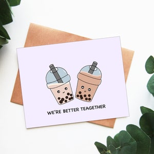 May include: A greeting card with two cartoon bubble tea cups, each with a smiling face and boba pearls. The card has the text "WE'RE BETTER TEAGETHER" and is on a light purple background, with a brown envelope behind it.