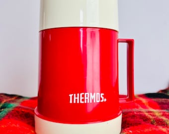 May include: A red thermos with a white lid and handle. The thermos has the word "THERMOS." printed on the side.