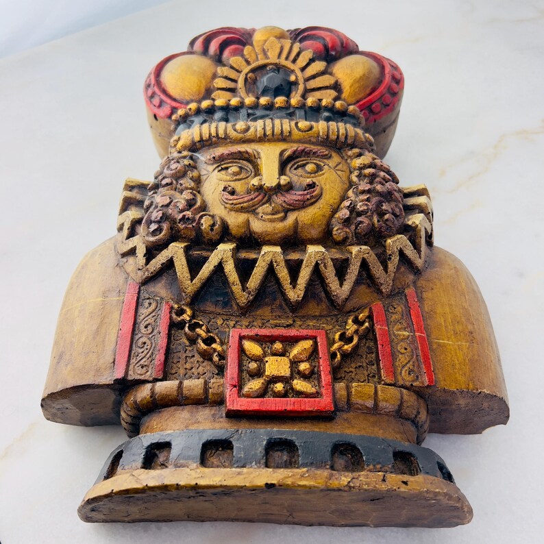 May include: A wooden figurine of a king with a gold crown, red and gold trim, and a moustache. The figurine is painted in shades of brown, gold, and red.