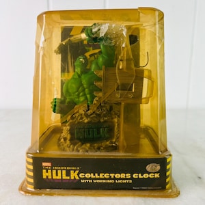 May include: The Incredible Hulk Collectors Clock with working lights. The clock features a green Hulk figurine in a clear plastic case. The clock has a brown base with the word "Hulk" on it. The clock is in a yellow and black box.