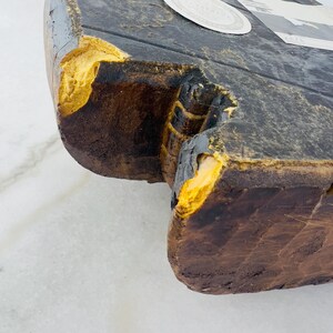 May include: Close-up of a wooden block with a dark brown finish and yellowed edges. The block has a carved design on one side and a smooth surface on the other.