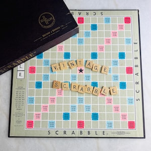 May include: Vintage Scrabble board game with wooden letter tiles spelling "VINTAGE SCRABBLE". The game board is green and white with colored squares for bonus points. The black box lid is visible with the Selchow & Righter Co. logo.