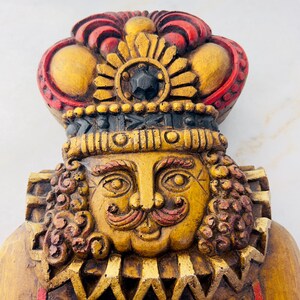 May include: A wooden figurine of a king with a gold and red crown, a gold face with a red moustache and eyebrows, and a gold and red patterned collar.