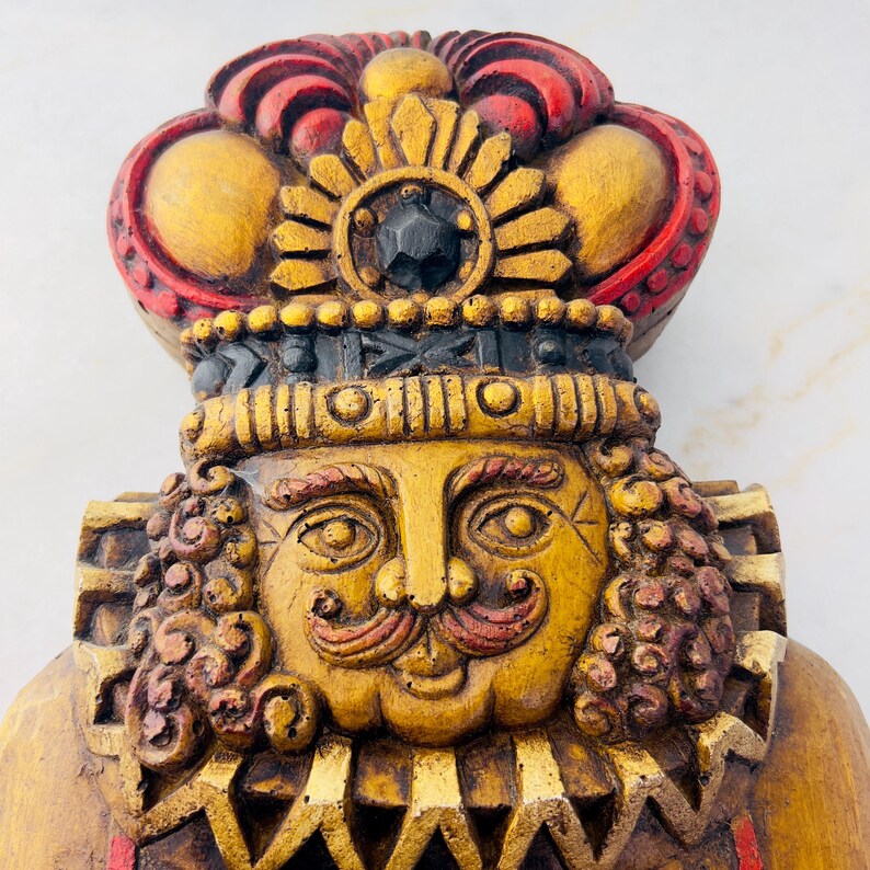 May include: A wooden figurine of a king with a gold and red crown, a gold face with a red moustache and eyebrows, and a gold and red patterned collar.
