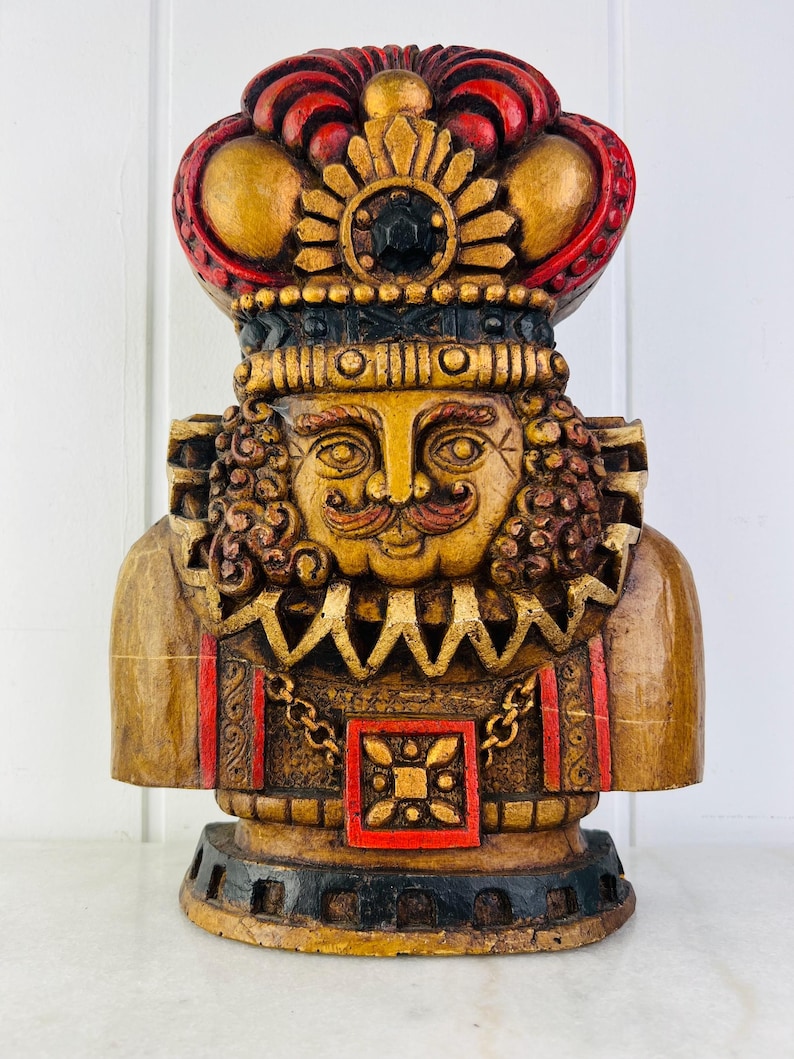 May include: A wooden figurine of a king with a red and gold crown, a gold chain, and a red and gold patterned chest. The figurine is painted in shades of gold, red, and black.