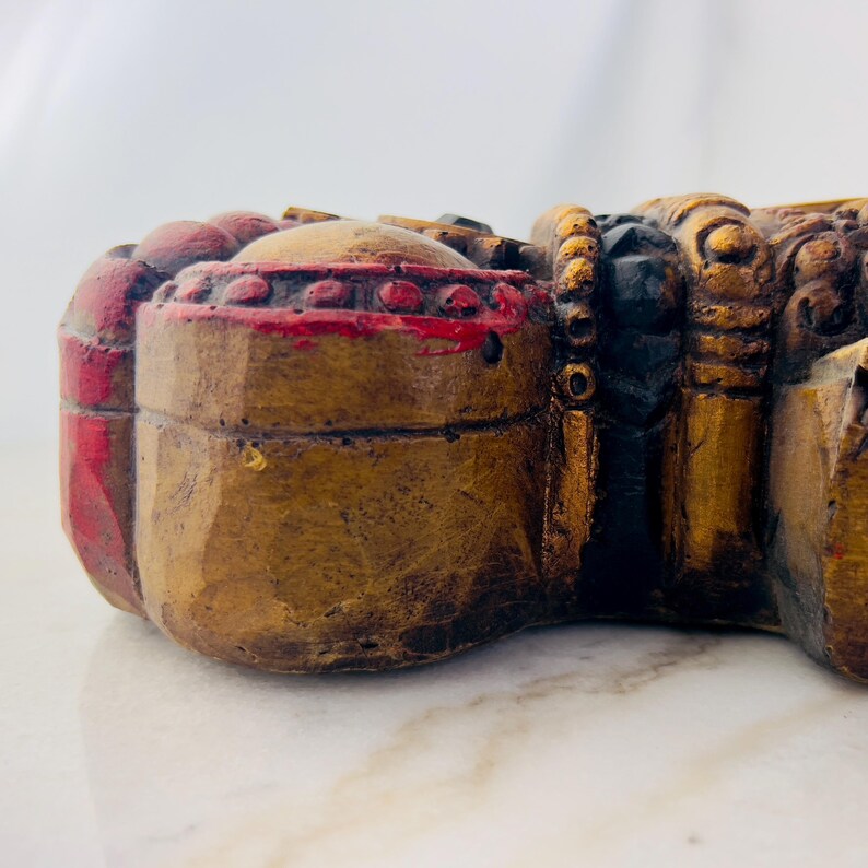 May include: A gold and red wooden sculpture with intricate details. The sculpture is carved in the shape of a mythical creature with a large head and a long tail.