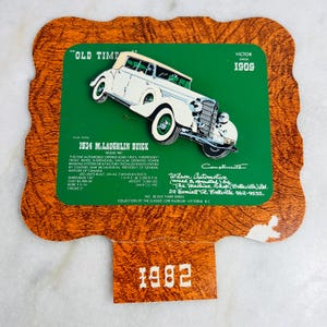 May include: A vintage sign with a green background, showcasing a 1934 McLaughlin Buick car illustration. The sign includes details about the car, the year 1982, and the phrases "Old Time" and "Victor Since 1909". The sign is in a decorative shape.