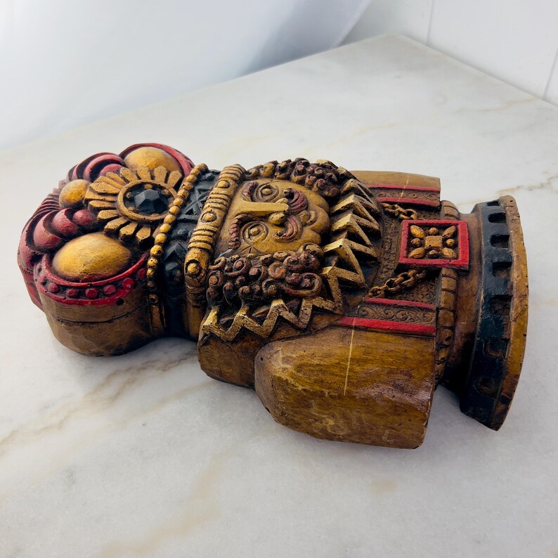 May include: A wooden nutcracker figurine with a gold and red crown, a detailed face, and a gold and red patterned body.