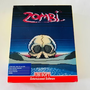 Puede incluir: Una caja de videojuego vintage de "Zombi" con gráficos pixelados. La ilustración de la caja muestra una calavera sobre un fondo azul y negro, con el título en rojo. El logotipo de Ubi Soft y los requisitos del juego también son visibles.