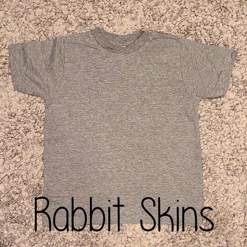 Puede incluir: Una camiseta gris jaspeada con el texto "Rabbit Skins" impreso en la parte inferior.