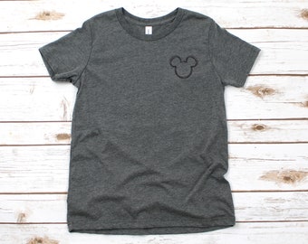 Könnte beinhalten: Ein dunkelgraues T-Shirt mit einer schwarzen Mickey-Maus-Kopf-Silhouette, die auf die linke Brust gestickt ist.