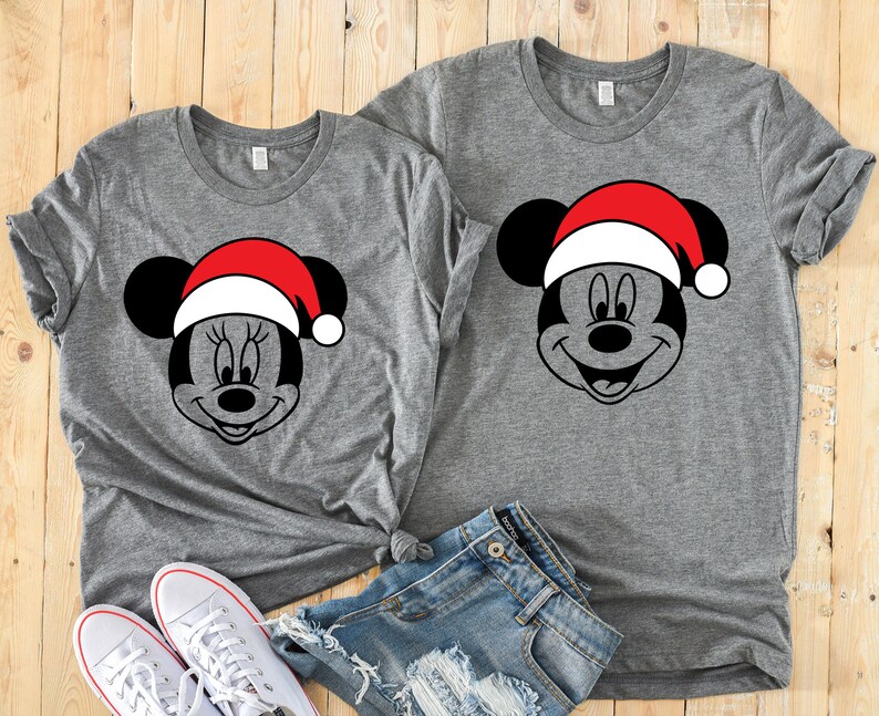 May include: Two gray t-shirts with a black and white image of Mickey Mouse wearing a red Santa hat.