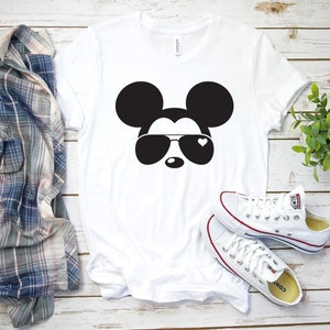 Op de afbeelding: Wit T-shirt met een zwart-witte afbeelding van Mickey Mouse met een zonnebril met een hartje op &eacute;&eacute;n lens.