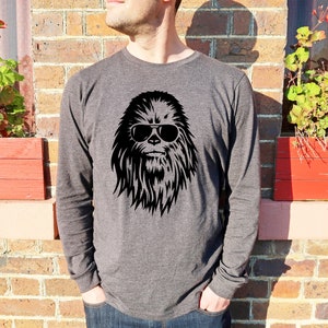 May include: A dark grey long-sleeved shirt featuring a black graphic of a furry creature wearing sunglasses. The creature has a long, bushy beard and a serious expression.