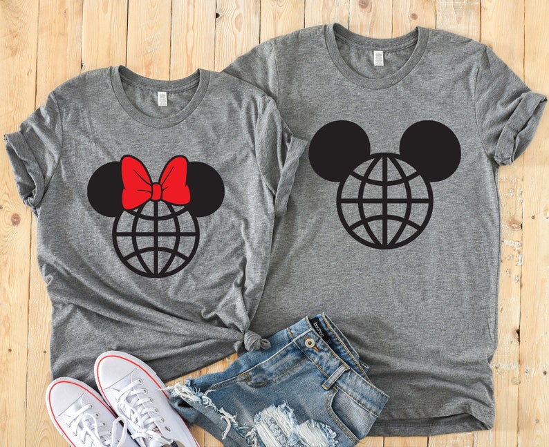 K&ouml;nnte beinhalten: Zwei graue T-Shirts mit einem schwarzen und wei&szlig;en Globus-Design in Mickey-Maus-Ohren. Ein Shirt hat eine rote Schleife oben auf den Ohren.