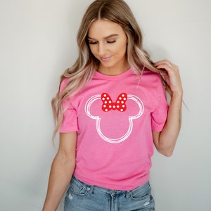 Op de afbeelding: Een roze T-shirt met een witte omtrek van Mickey Mouse's hoofd en een rode strik met witte stippen.