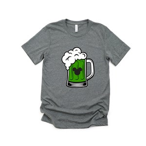 Puede incluir: Una camiseta gris jaspeada con una jarra de cerveza verde con espuma blanca y una cabeza de Mickey Mouse negra en la jarra.