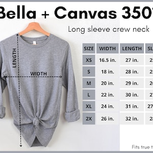 Pode incluir: Uma camiseta cinza de manga comprida e gola redonda com uma tabela de tamanhos que mostra as medidas em polegadas. A tabela inclui os tamanhos XS, S, M, L, XL e 2X. A camiseta &eacute; Bella + Canvas 3501.