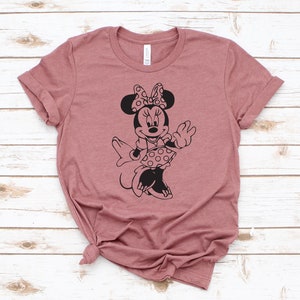 May include: A mauve t-shirt with a black silhouette of Minnie Mouse wearing a polka dot dress and a bow.