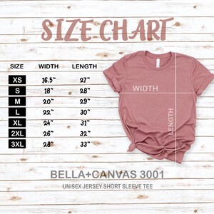 May include: A size chart for a unisex jersey short sleeve tee, with measurements in inches. The chart lists sizes XS to 3XL, with corresponding width and length measurements. A dusty rose colored t-shirt is displayed on a wooden background.