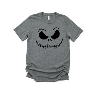 K&ouml;nnte beinhalten: Ein heidefarbenes T-Shirt mit einem schwarzen Jack Skellington Gesichtsmotiv.