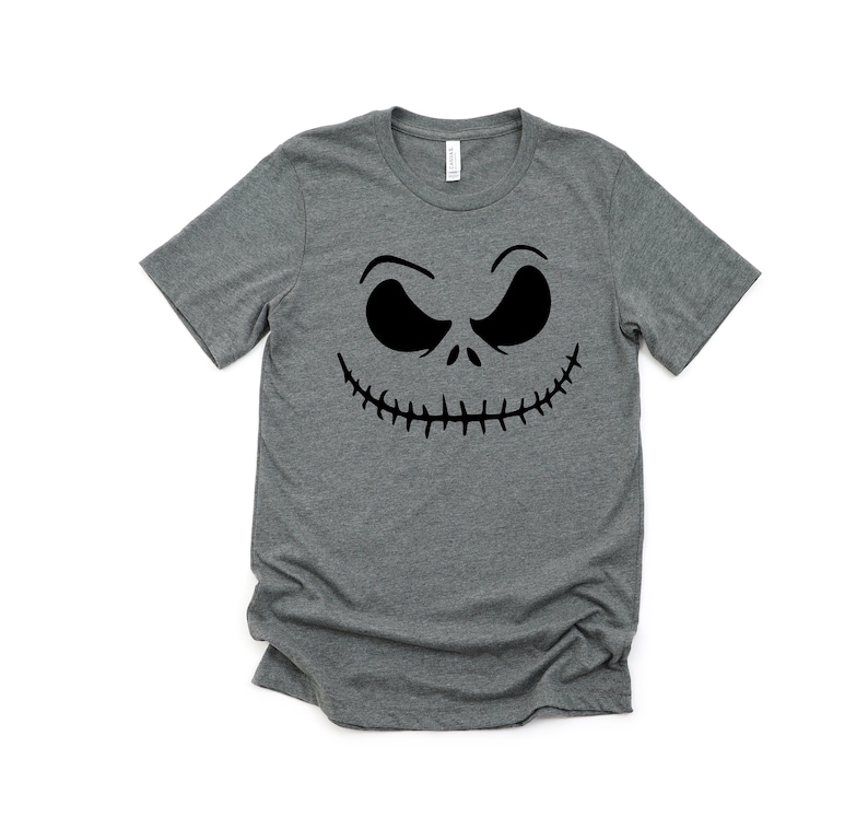 K&ouml;nnte beinhalten: Ein heidefarbenes T-Shirt mit einem schwarzen Jack Skellington Gesichtsmotiv.
