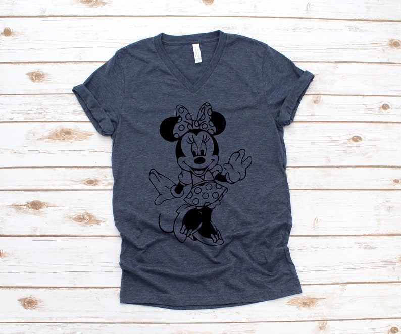 May include: A dark blue V-neck t-shirt with a black and white silhouette of Minnie Mouse wearing a polka dot dress and a bow.