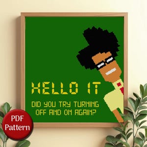 Peut inclure: Motif de point de croix encadré dans un cadre en bois marron clair. L'œuvre présente un personnage pixélisé avec des cheveux noirs et des lunettes, regardant de droite. Le texte dit "HELLO IT, DID YOU TRY TURNING OFF AND ON AGAIN?"