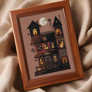 A framed cross-stitch image depicting a spooky, multi-level house with various architectural elements and a full moon in the sky.