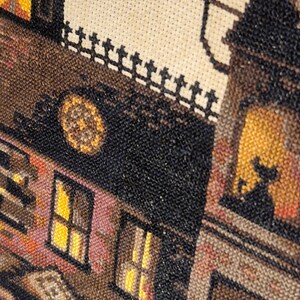 The image is a close-up of a cross-stitch pattern depicting a building with a clock and a cat silhouette.