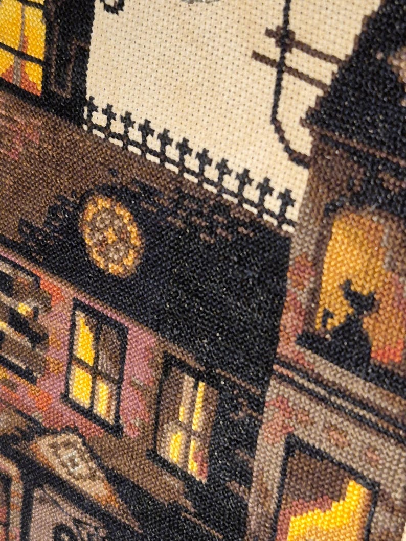 The image is a close-up of a cross-stitch pattern depicting a building with a clock and a cat silhouette.