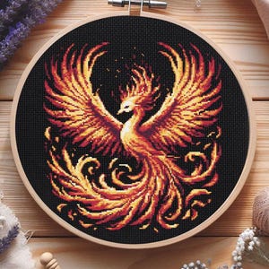 Könnte beinhalten: Ein Kreuzstich-Stickrahmen mit einem farbenfrohen Phönix-Motiv. Der Phönix ist mit orangefarbenen, gelben und roten Federn dargestellt und vor einem schwarzen Hintergrund platziert.