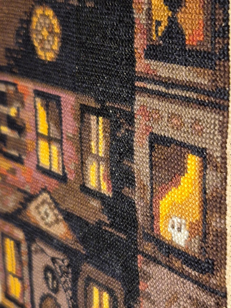 The image is a close-up of a colorful, textured tapestry or textile featuring a variety of patterns and designs, including a building with a clock and a yellow object.