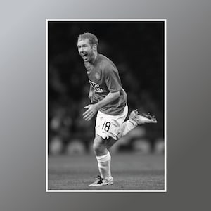 May include: A black and white photo of a soccer player wearing a red jersey with the number 18 on it. The player is running and kicking the ball with his right foot. He is celebrating a goal.