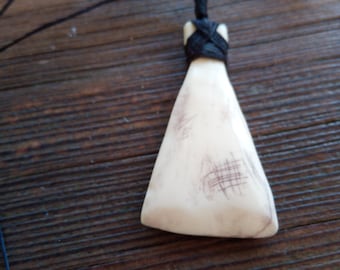 May include: A white bone pendant with a black braided cord. The pendant is shaped like a triangle with rounded edges and has a textured surface.
