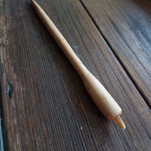 Könnte beinhalten: Ein Holzstab mit einer spitzen Spitze. Der Stab ist hellbraun und hat eine glatte Oberfläche. Er liegt auf einer Holzoberfläche.