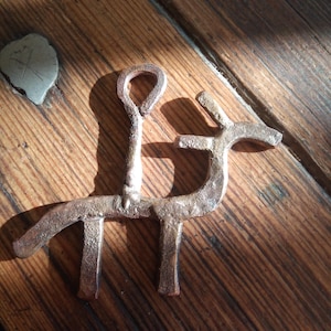 May include: A metal pendant shaped like a person riding a horse. The pendant is made of dark metal and has a rustic finish.