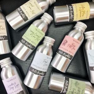 May include: A collection of silver metal diffuser refill bottles with various labels and scents. The labels feature different floral and botanical designs with names like "Blooper", "Bigwig", "Blousey", and "Bijou".
