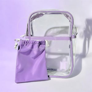 Peut inclure: Un sac transparent rectangulaire avec une bordure violette et une pochette assortie &agrave; cordon de serrage. Le sac a une poign&eacute;e blanche et une fermeture &eacute;clair argent&eacute;e. La pochette est de couleur violette unie. Le sac mesure environ 25 cm de haut et 20 cm de large.